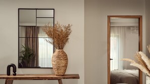 A modern room with a wooden desk, a large mirror, and a vase with dried plants.