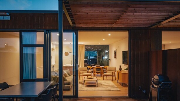 Ein modernes Interieur mit Essbereich, Wohnzimmer mit Sofa und Sesseln, und eine durchgehende Tür sichtbare Küche.