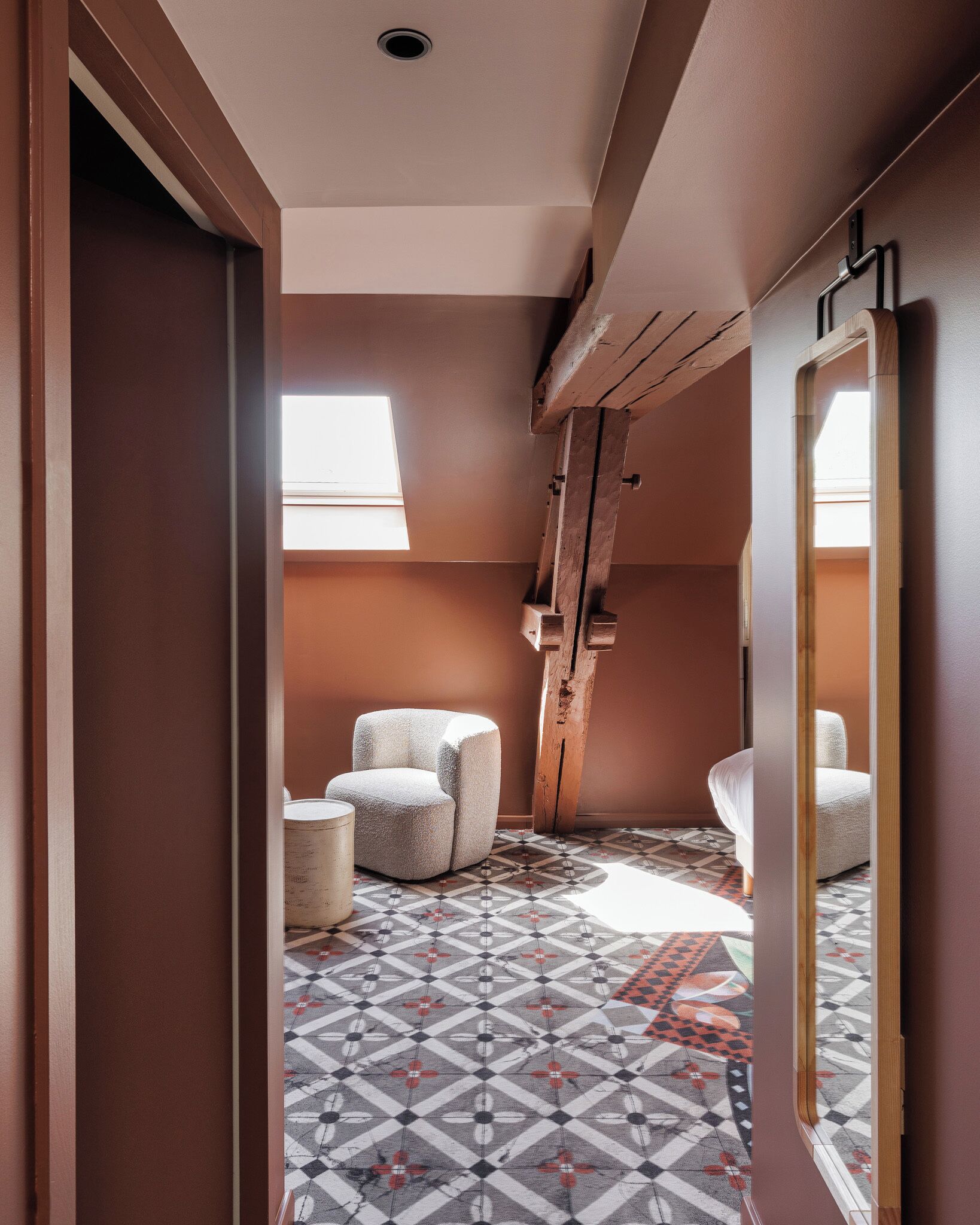 A hallway with a patterned floor, two armchairs, a wooden beam, and a large mirror.