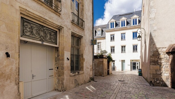 Una estrecha calle adoquinada con edificios históricos, una entrada porticada y un cielo despejado.