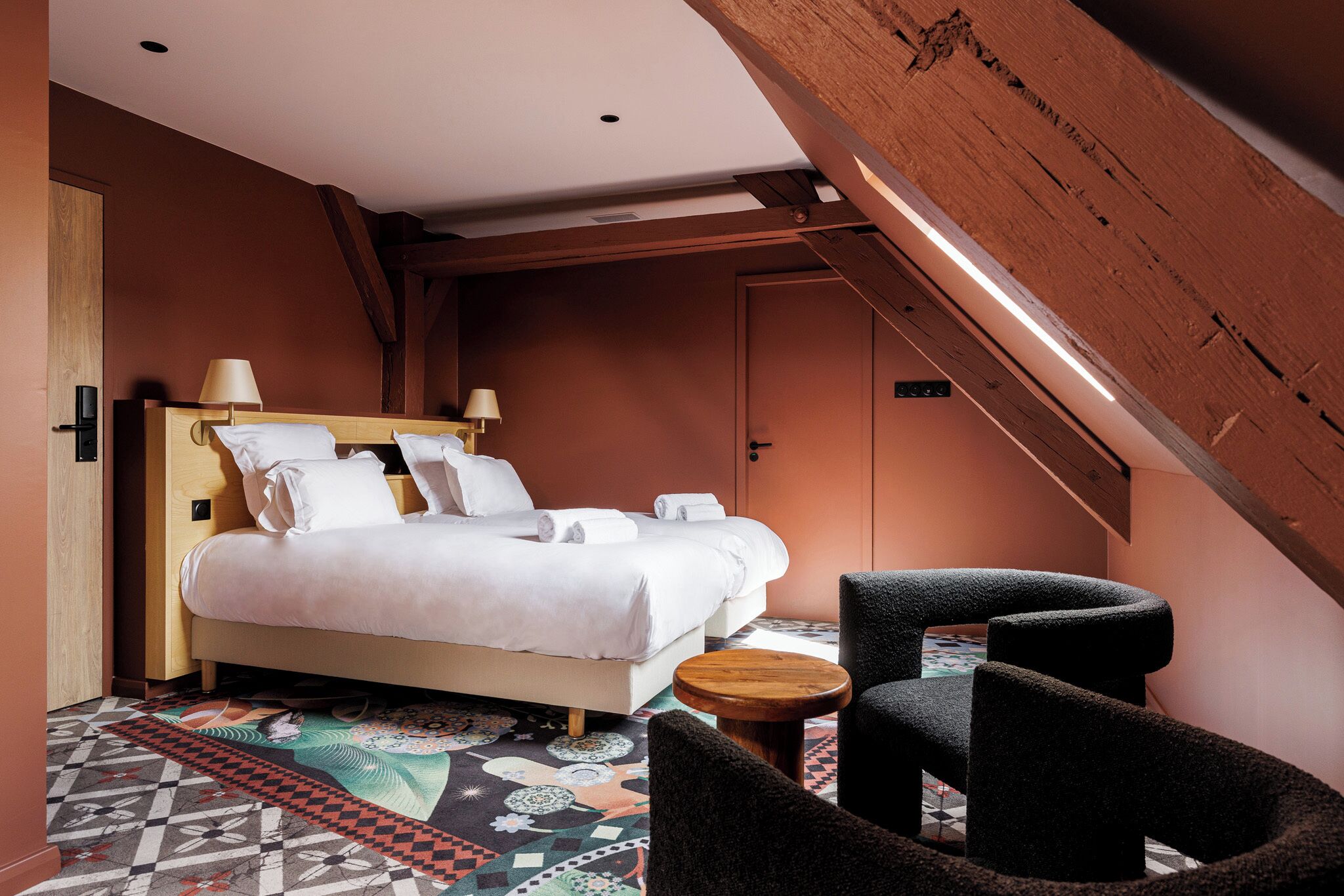 A bedroom with a bed, two chairs, a small table, and a patterned rug.