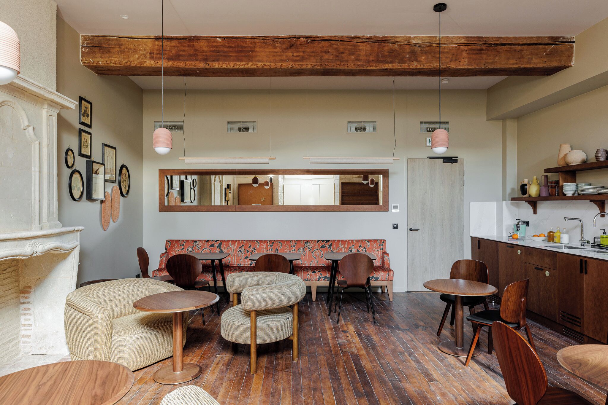 A cozy interior with a wooden ceiling, a dining area with round tables and chairs, a patterned sofa, and a kitchen area with wooden cabinets and a sink.