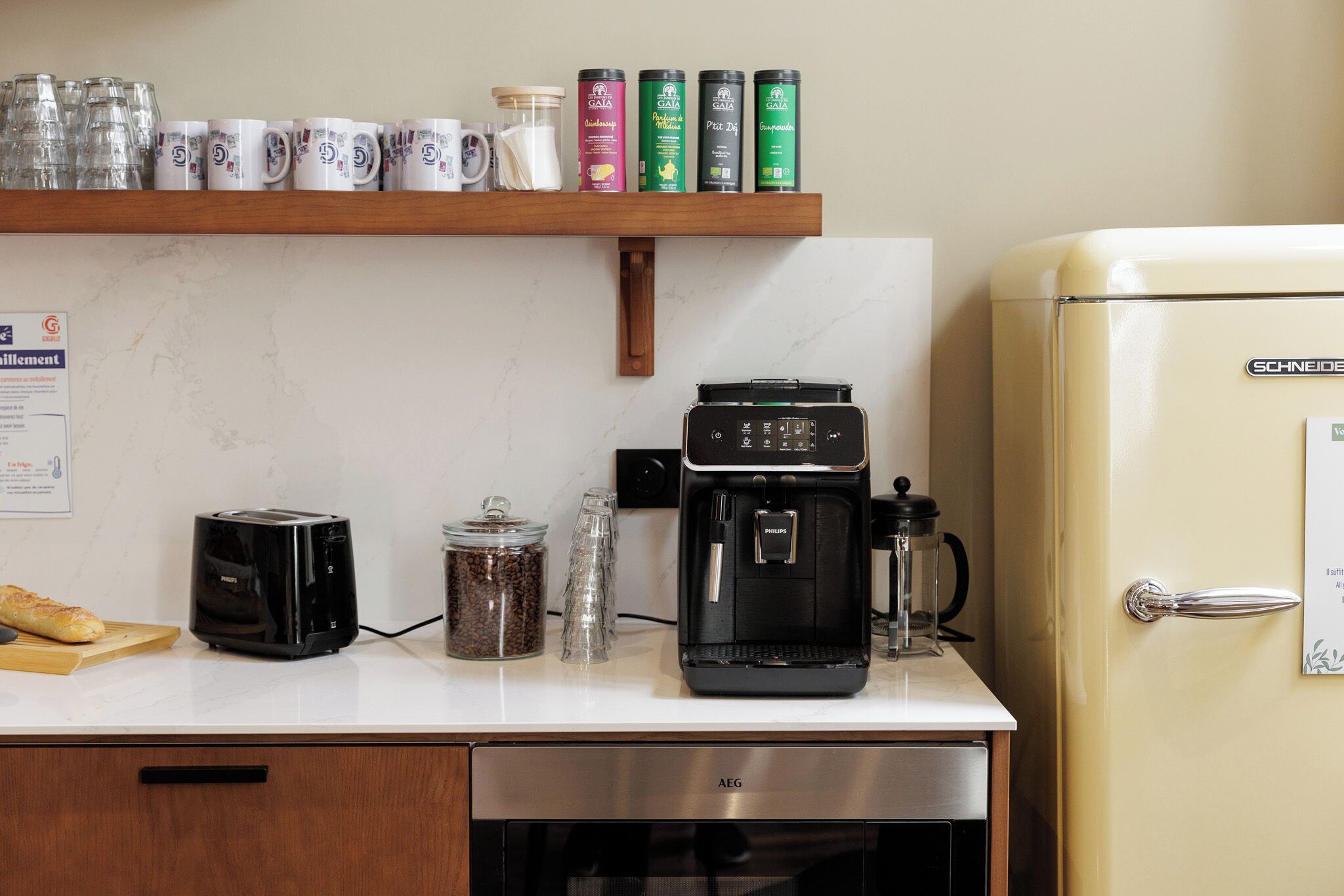 A kitchen with a white countertop, a toaster, a coffee maker, a jar of coffee beans, and a refrigerator.