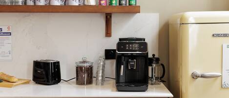 A kitchen with a white countertop, a toaster, a coffee maker, a jar of coffee beans, and a refrigerator.