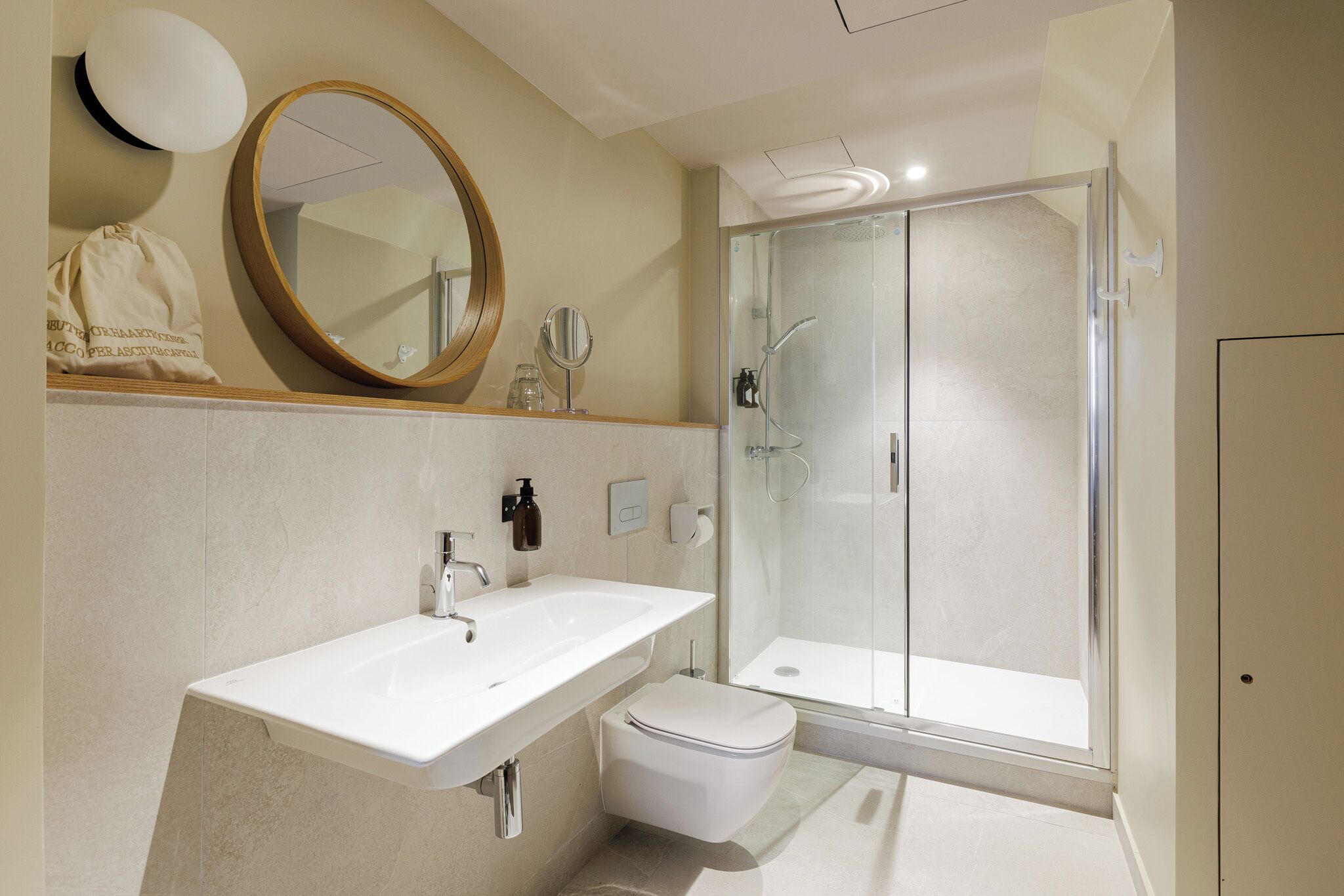 A modern bathroom with a white sink, a toilet, a glass-enclosed shower, and a large mirror.