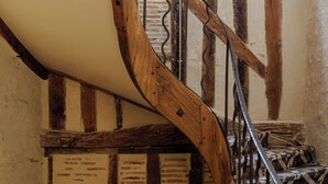 Una escalera espiral de madera con barandilla de metal, que conduce a una habitación con paredes de ladrillo visto y un ventanal.