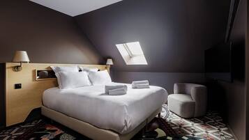 Una habitación de hotel moderna con una cama grande, un sillón pequeño, un tragaluz y un televisor de pantalla plana.