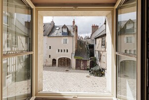 Un patio adoquinado con edificios de estilo europeo tradicional, una escalera visible y un marco de ventana.