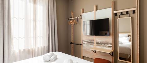 A hotel room with a bed, a TV, a mirror, and a window with curtains.