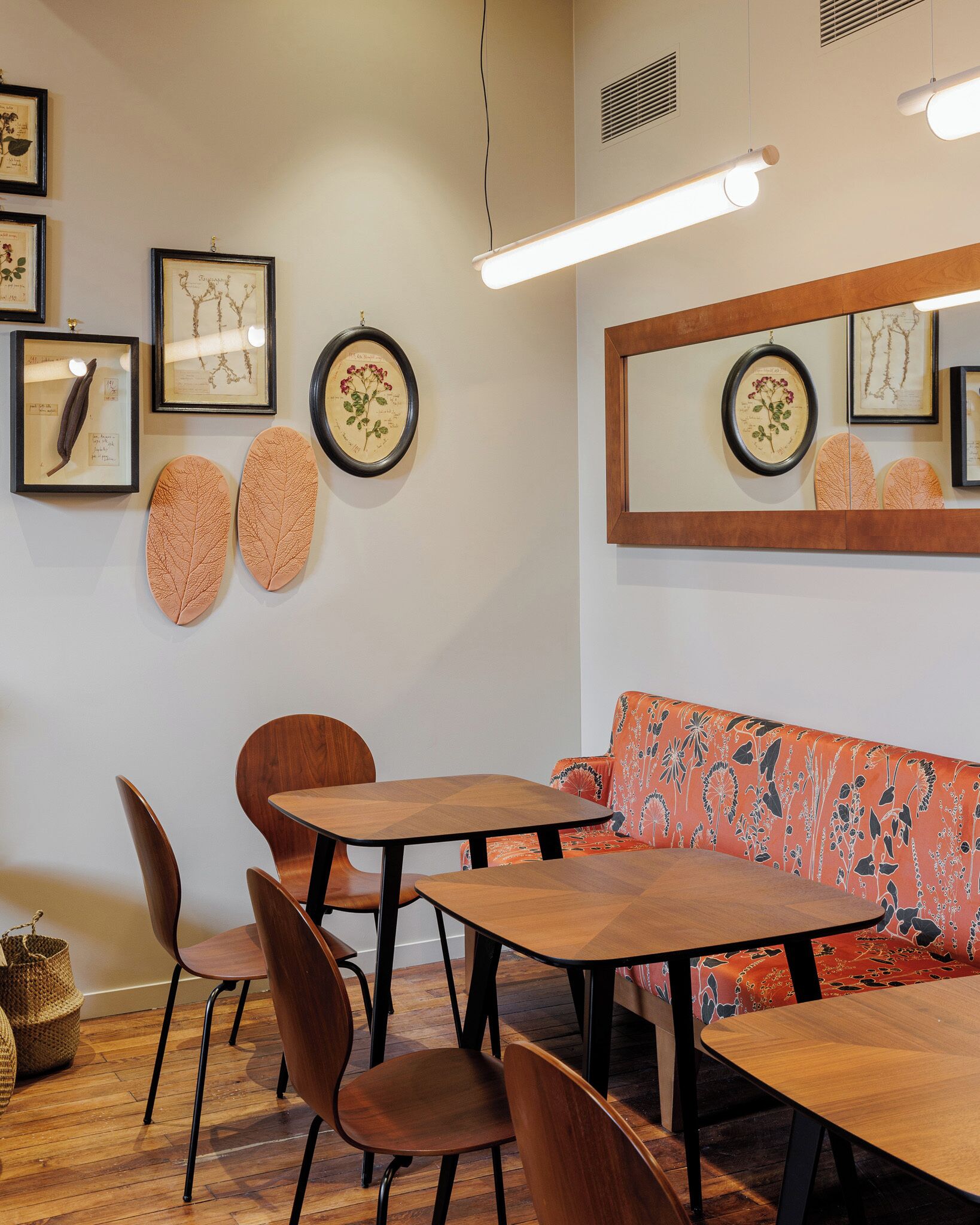 A modern dining area with wooden furniture, framed botanical prints on the walls, and a large mirror reflecting the space.