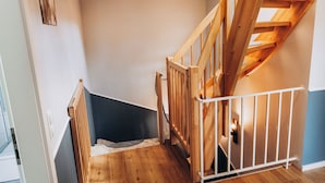 Una escalera de madera con barandilla blanca, pared oscura y suelo de color claro.