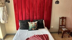 A bed with a white sheet, red curtains, and multiple pillows. There is a wooden chair with a tray and a white object on it. - The White House  (Phalaborwa)