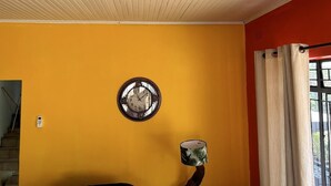 A room with a yellow wall, a round wall clock, a telephone, and a window with curtains. - The White House  (Phalaborwa)