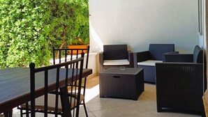 Patio esterno con tavolo e sedie, mobili in vimini e vista sul verde.