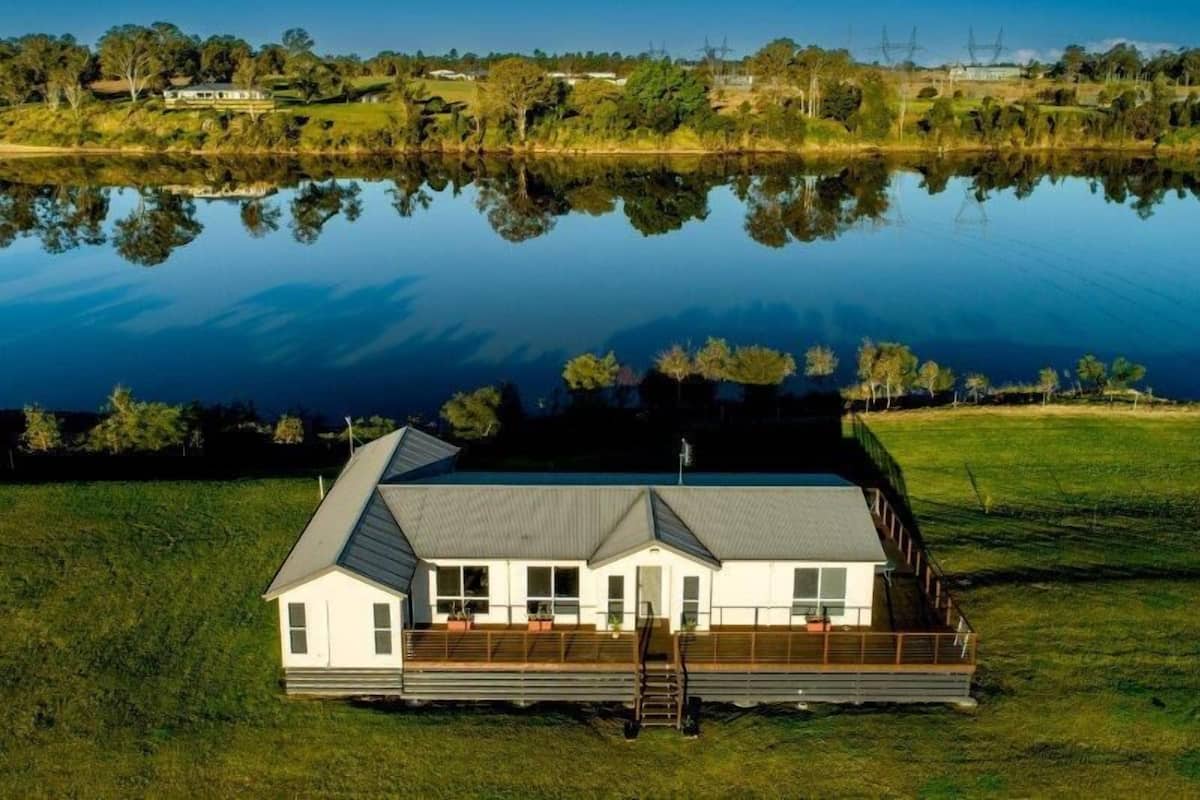 Een huis met een groot terras, een overdekte veranda en uitzicht op een meer.