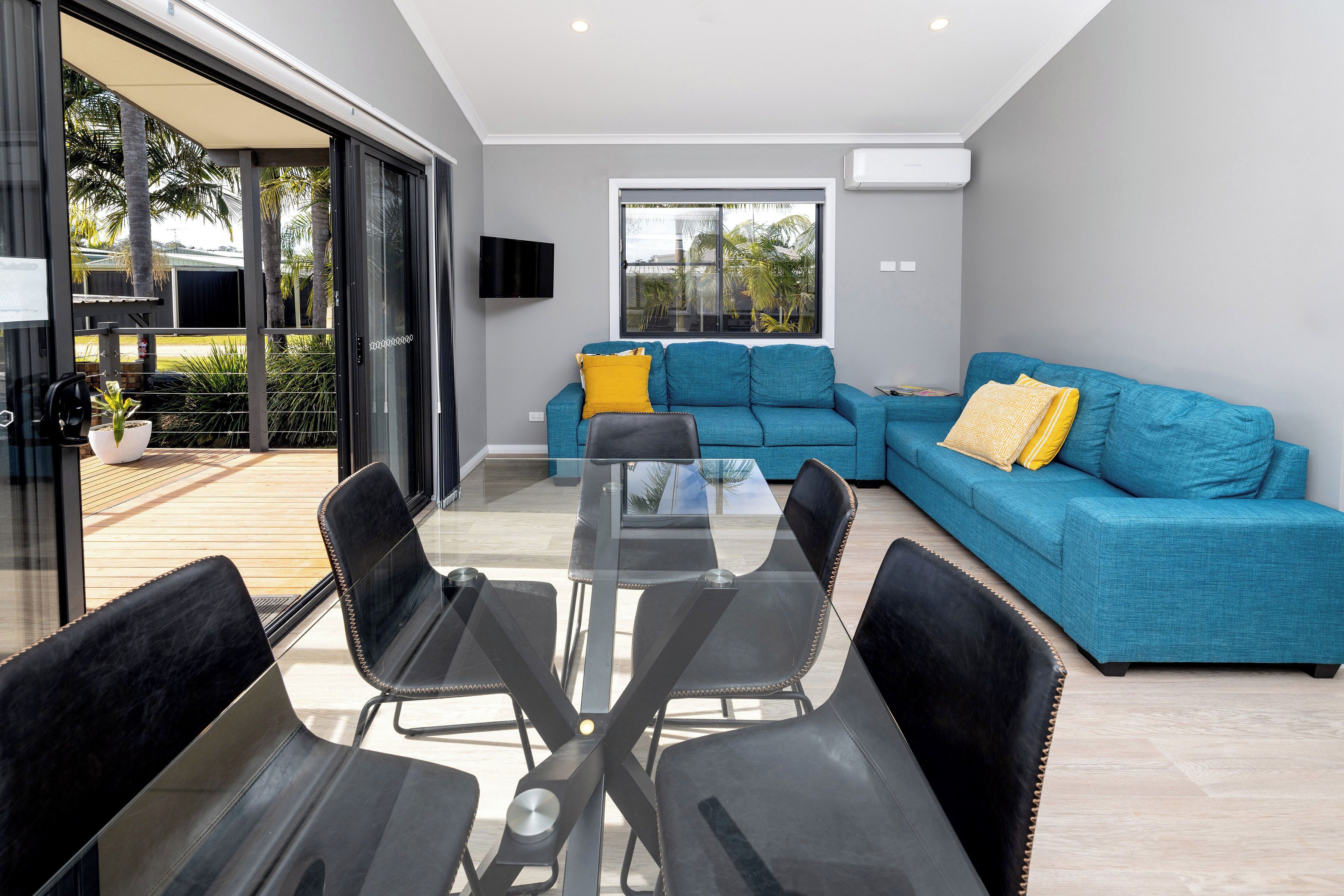 Una sala de estar moderna con un sofá azul, una mesa de comedor de vidrio y sillas negras.