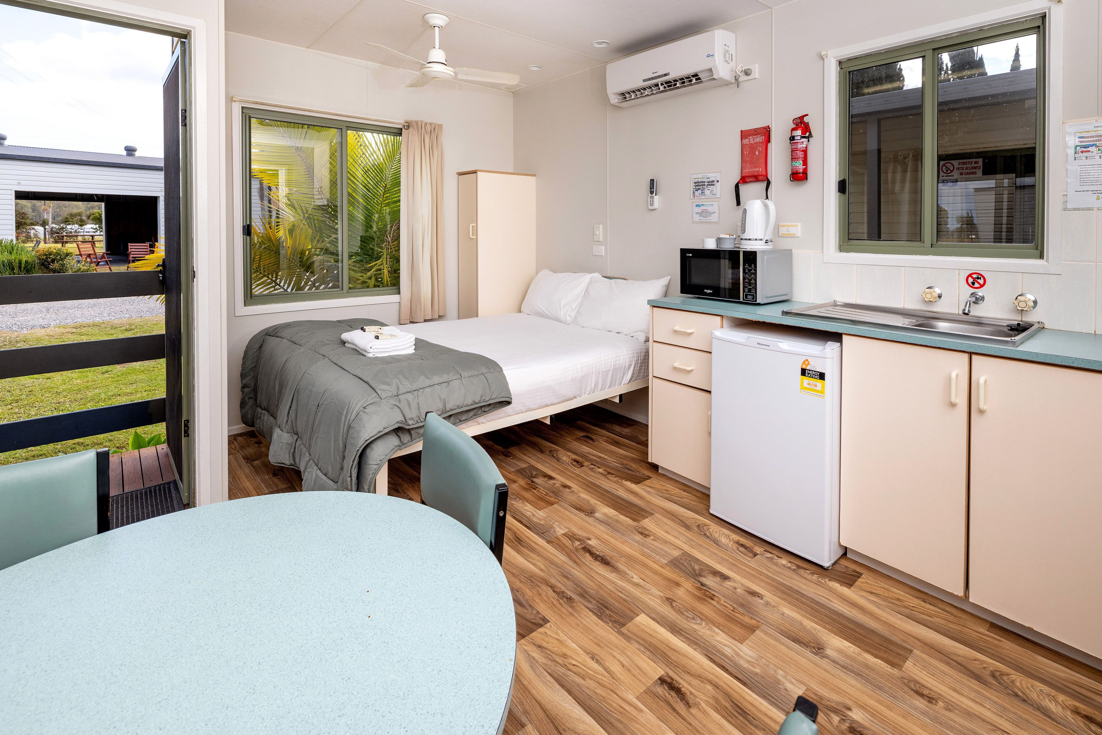 A compact room with a bed, a small kitchenette, a dining area, and a window with a view of the outside.