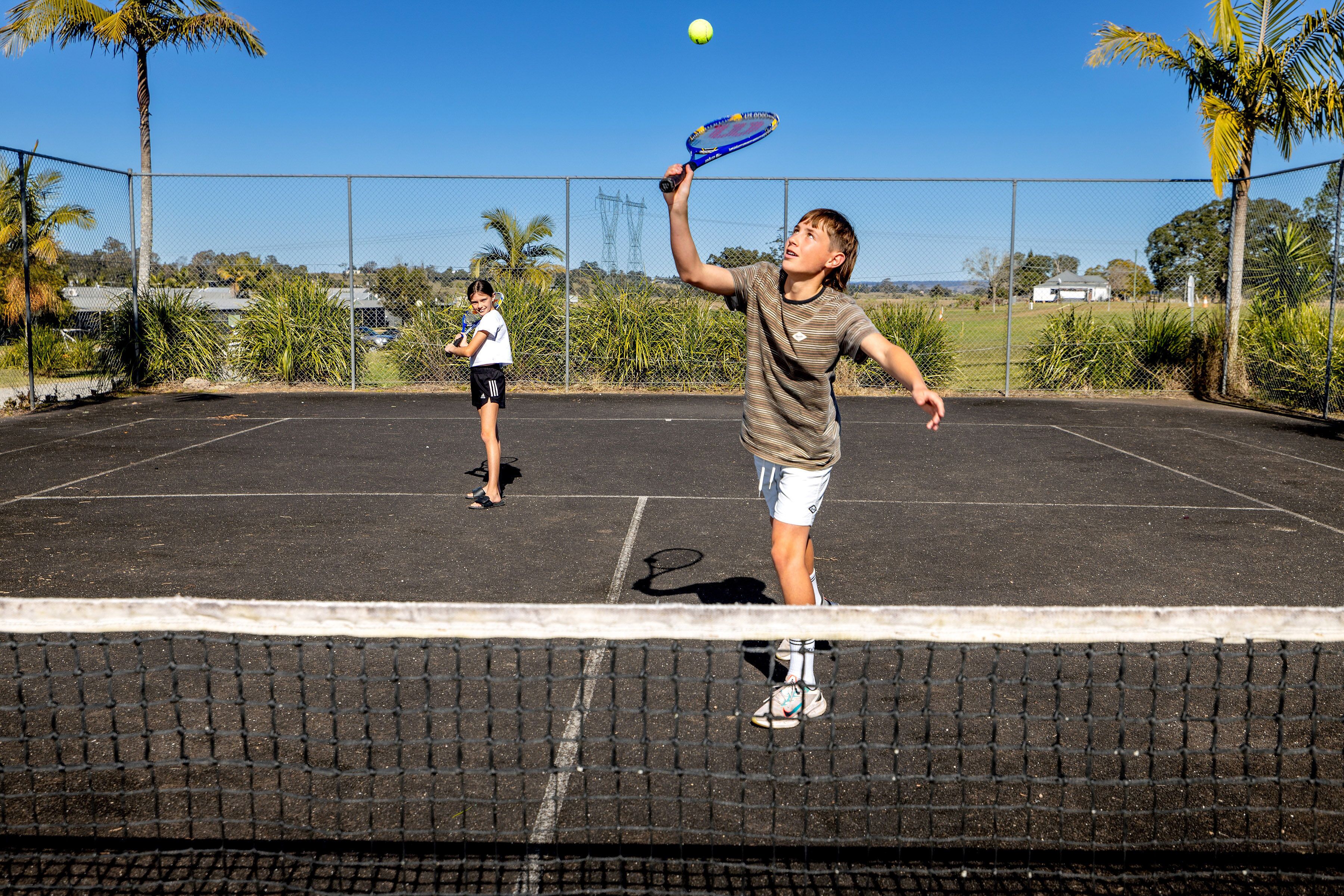 A tennis court with a net in the foreground and palm trees in the background.