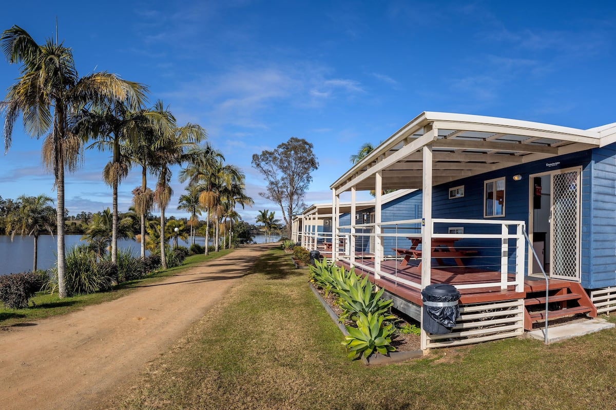 Een gelijkvloers blauw huis met een veranda, een houten terras en uitzicht op een meer.
