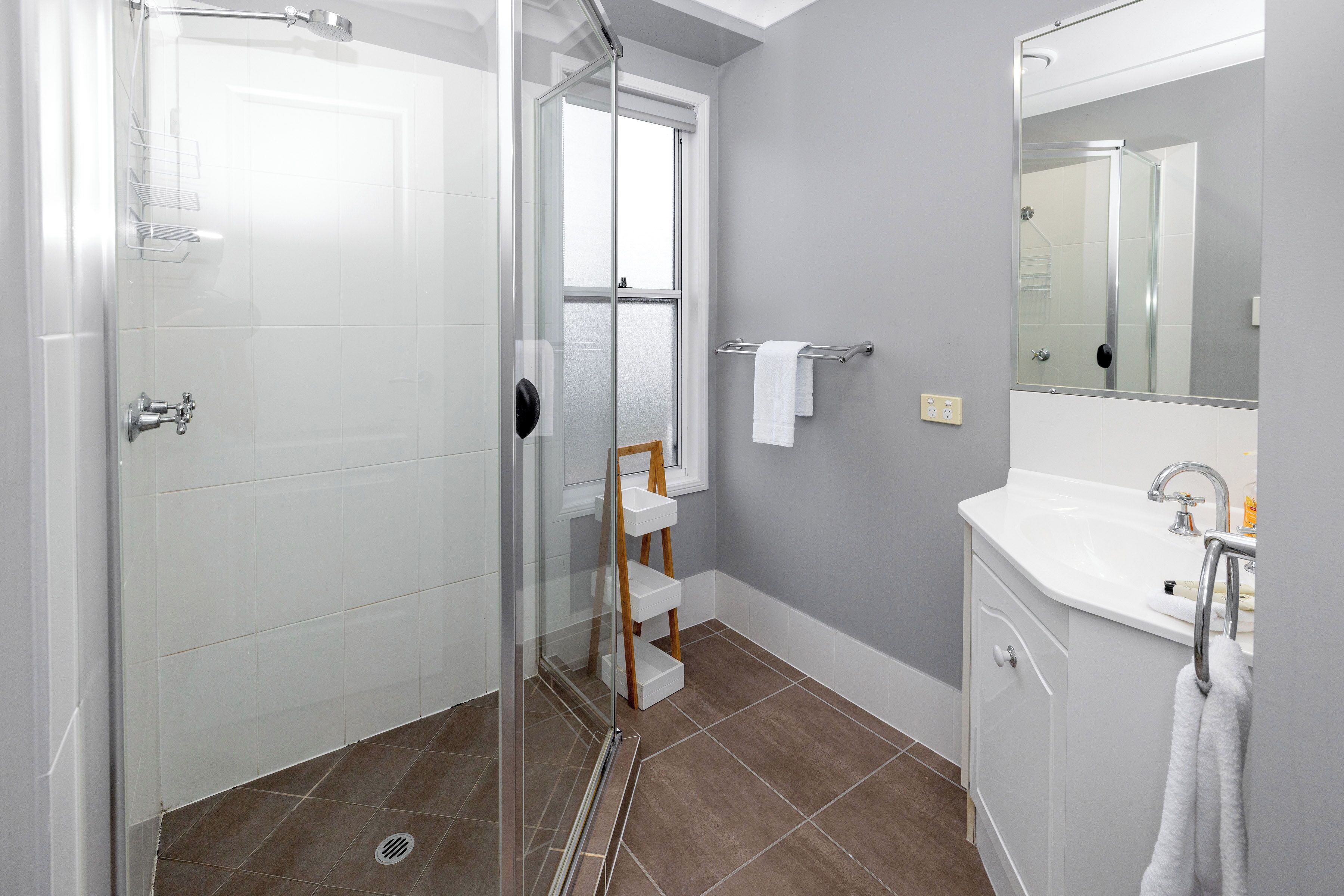 Un baño con cabina de ducha de vidrio, un lavamanos blanco y un espejo encima.