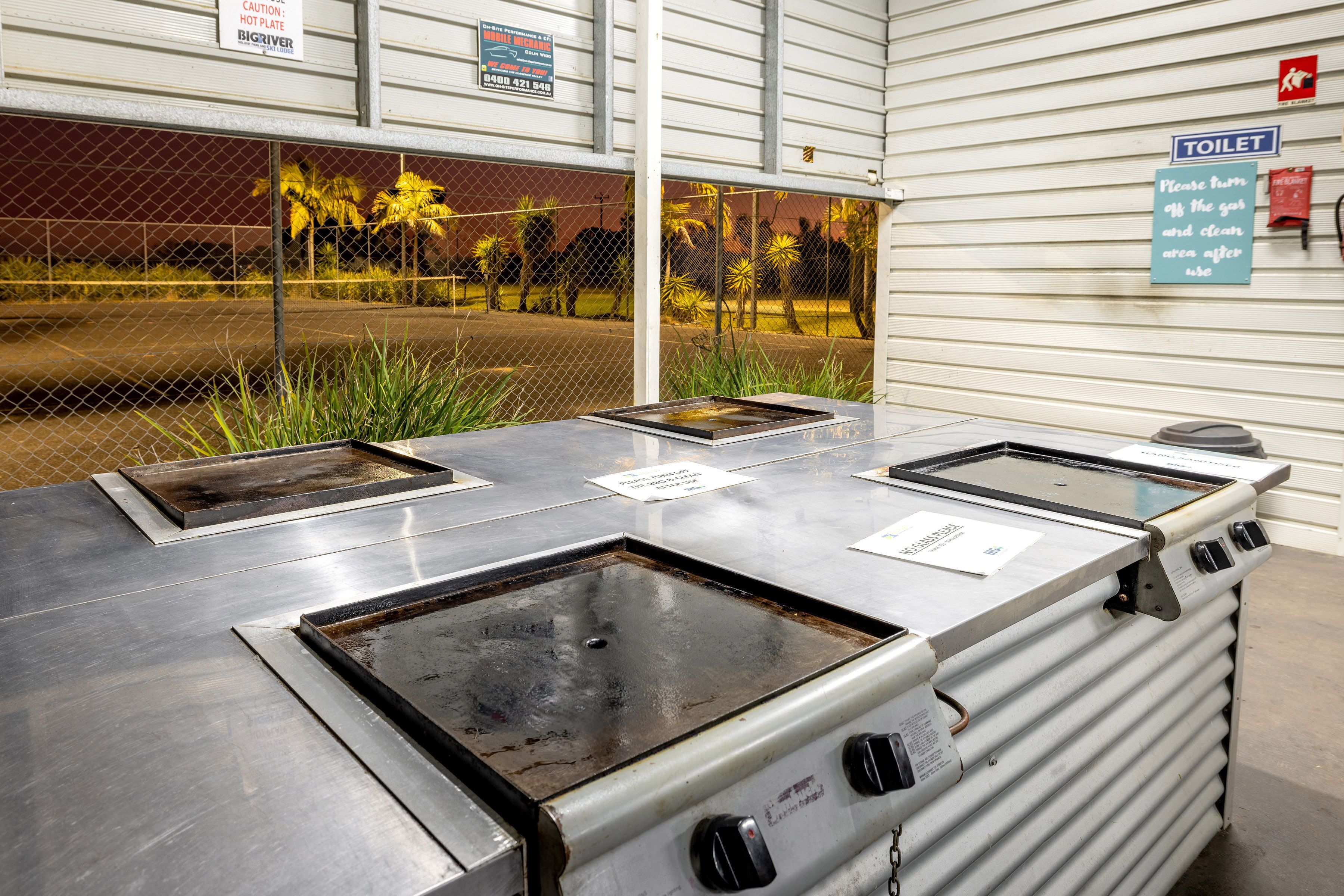 A kitchen area with four burners and a stove, a sign indicating a toilet, and a caution sign for a hot plate.