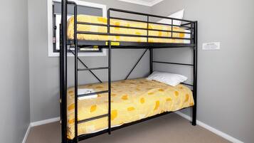 Un lit superposé avec une couvre-lit à motifs jaunes et des oreillers blancs, une fenêtre donnant sur un paysage agréable et un panneau d’avertissement de sécurité fixé au mur.