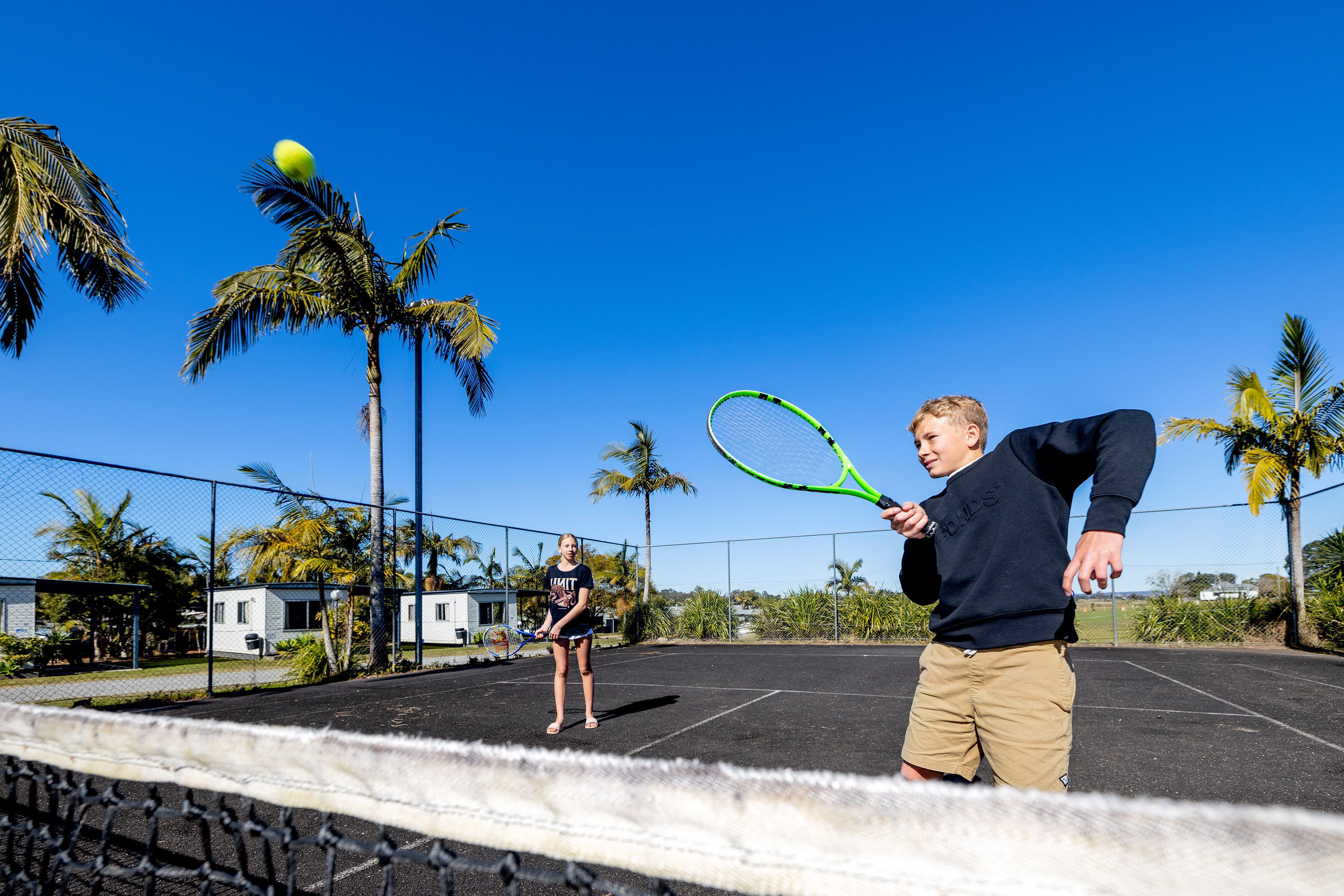 En tennisbane med net, palmer og en klar blå himmel.