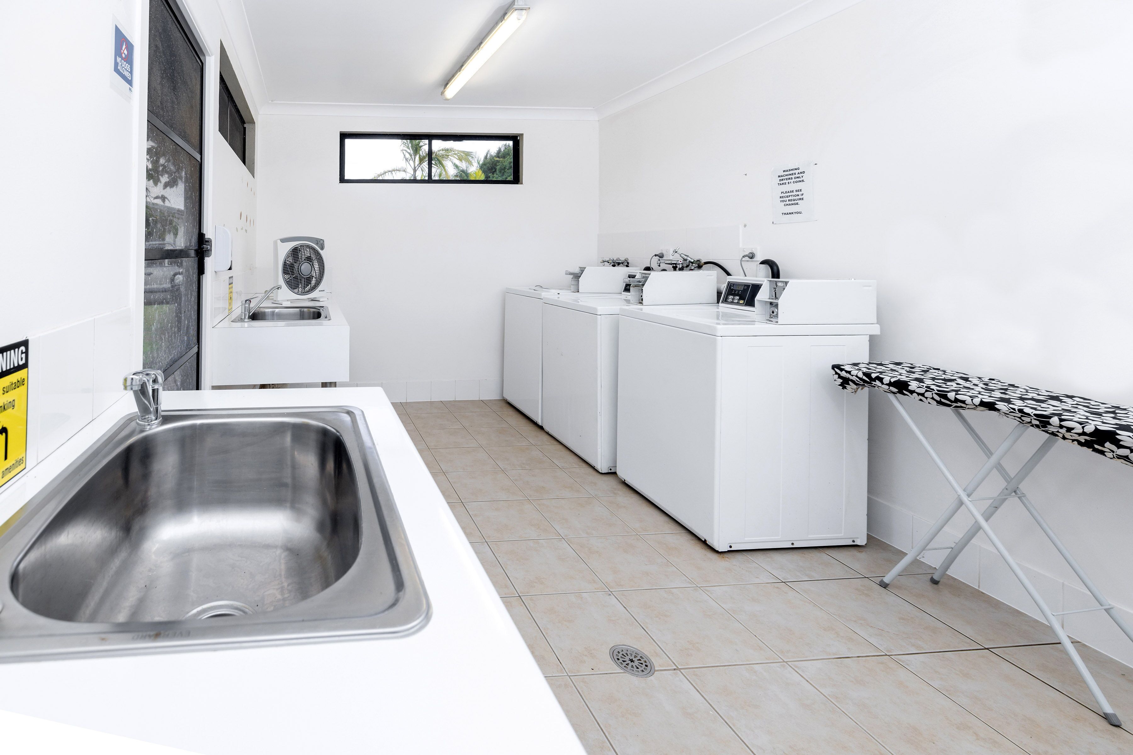 Een schone, witte wasruimte met een wasbak, wasmachines en een strijkplank.