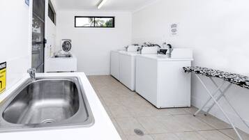 Een schone, witte wasruimte met een wasbak, wasmachines en een strijkplank.
