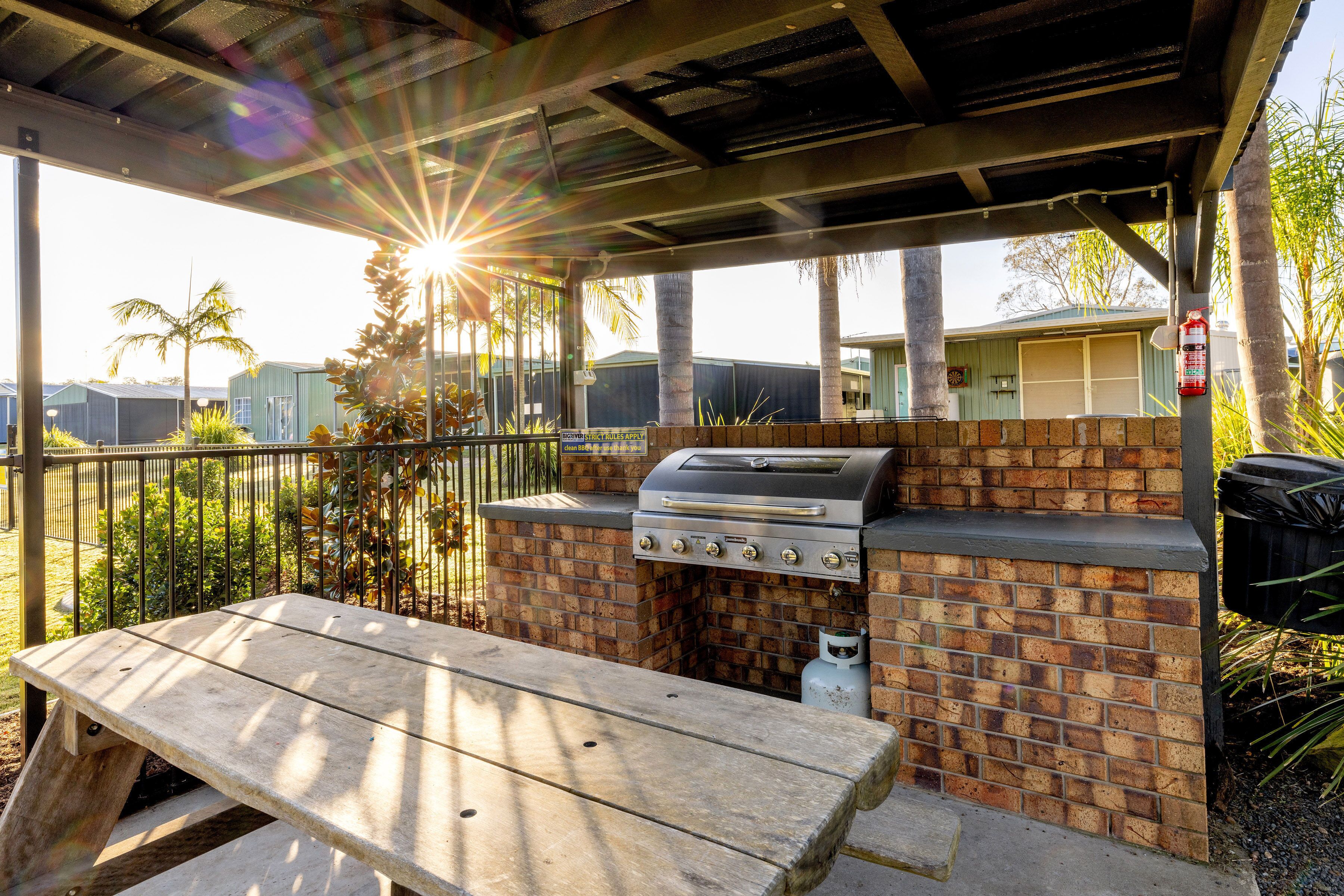 Un espace barbecue extérieur avec un gril en briques, une table en bois et un patio couvert.