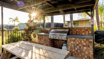 Un espace barbecue extérieur avec un gril en briques, une table en bois et un patio couvert.