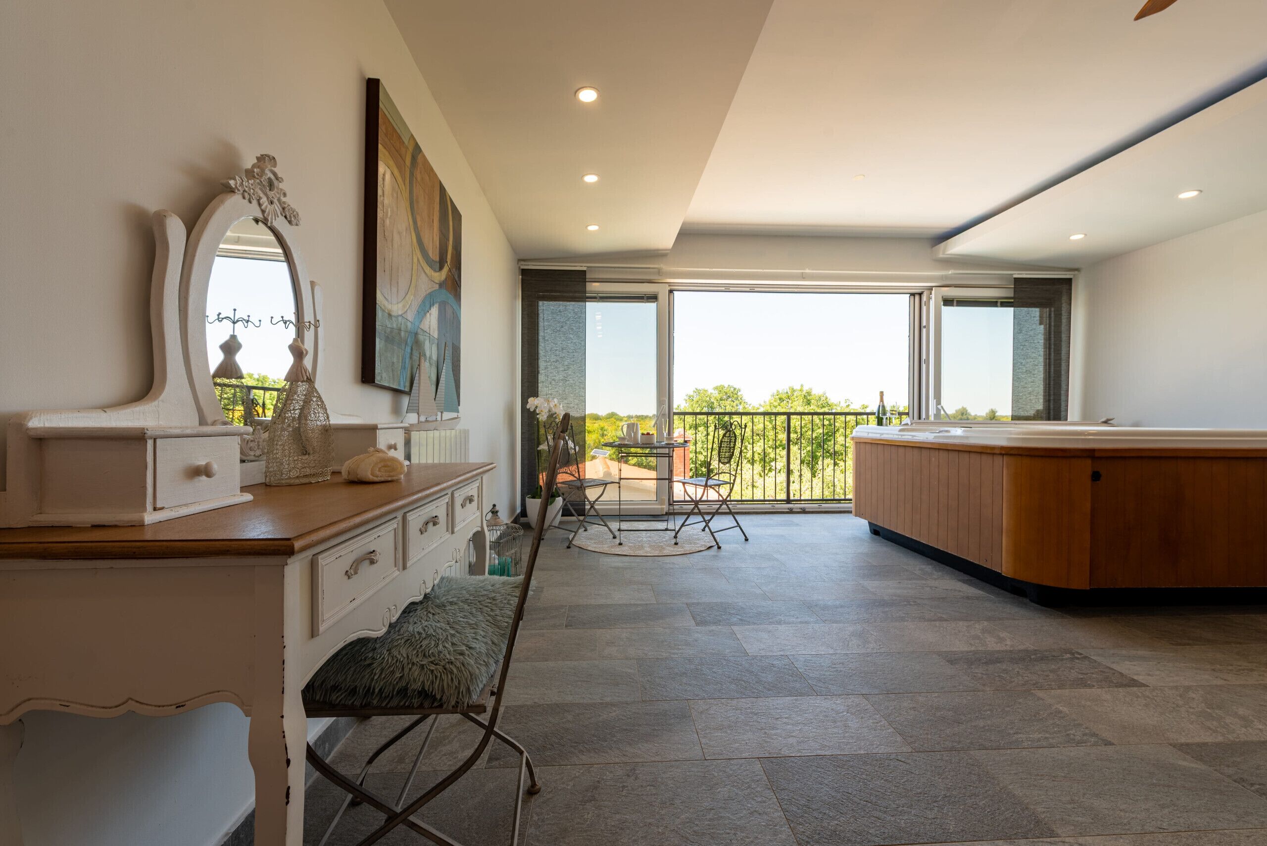 A spacious room with a large window, a wooden cabinet, a mirror, and a bench.