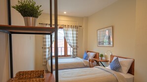 A bedroom with two beds, a wooden nightstand, a small table with a lamp, a potted plant, and a framed picture on the wall.