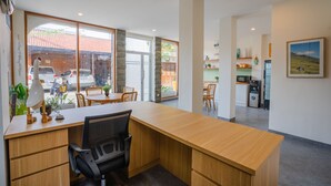 A modern office space with a wooden desk, black office chair, and large windows offering a view of the street.