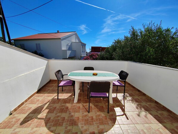 A patio with a round table and chairs, a tiled floor, and a white wall.