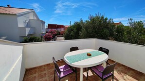 A round table with four chairs, a small table lamp, and a view of neighboring buildings and trees. - Poncho Apartment Close to Center (Novalja)