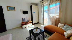 A living room with a sofa, a coffee table, a TV, a cabinet, and a door leading outside. - Poncho Apartment Close to Center (Novalja)