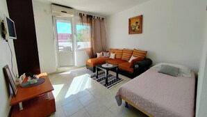 A room with a bed, a sofa, a desk, a television, and a window with curtains. - Poncho Apartment Close to Center (Novalja)