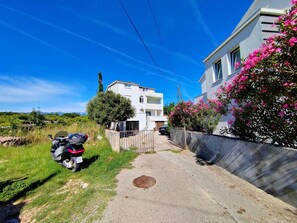 A residential area with a white building, a parked scooter, and a manhole cover on the ground.