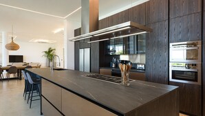 Une cuisine moderne dotée d’un grand îlot central, de meubles en bois foncé, d’appareils électroménagers en acier inoxydable et d’un luminaire suspendu.