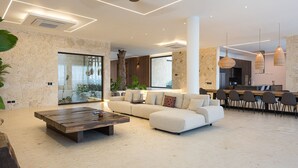 Un salon moderne avec un canapé d’angle, une table basse en bois et un coin repas comprenant des chaises et un bar.