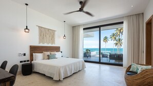 Une chambre d’hôtel moderne avec un grand lit, un ventilateur de plafond et une vue sur l’océan.