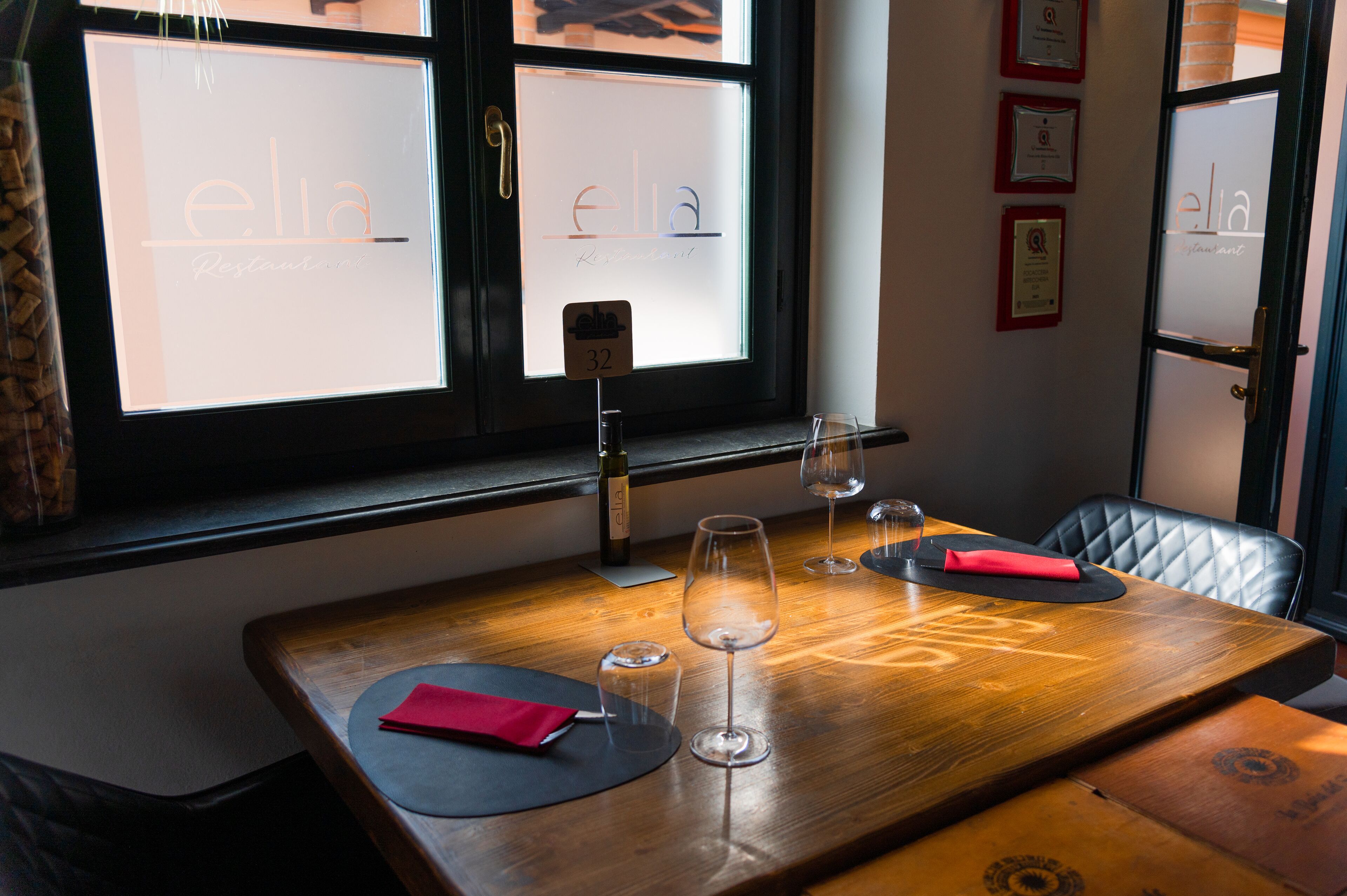 A restaurant interior with a wooden table, wine glasses, and a menu stand.
