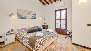A bedroom with a patterned bedspread, a nightstand, a wall-mounted lamp, a painting, and a wooden door. - Hotel la Pietra Restaurant (Fosdinovo)
