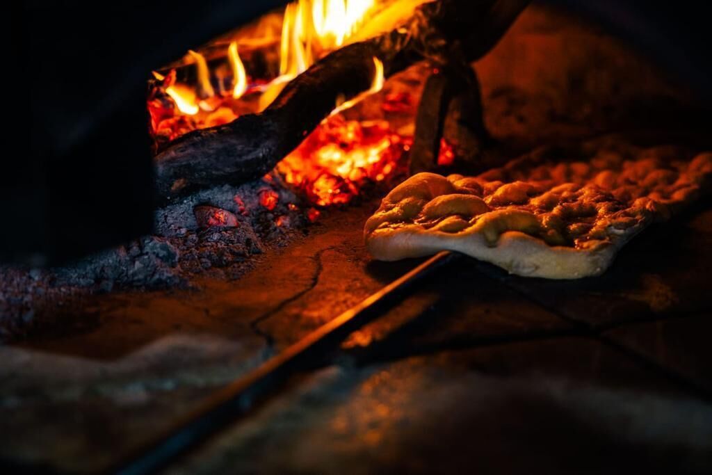 A pizza being cooked in a wood-fired oven with visible flames.