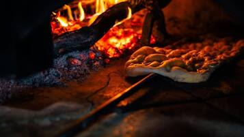 A pizza being cooked in a wood-fired oven with visible flames.