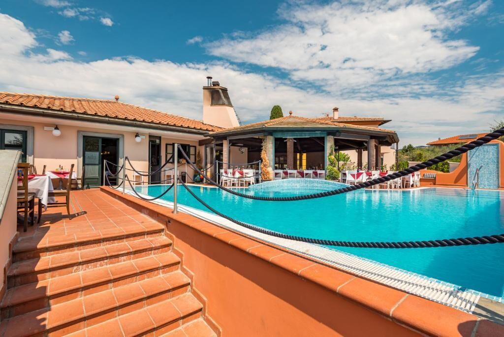 Una piscina en la azotea con cielo azul despejado, tejas de terracota y una zona de estar cubierta.