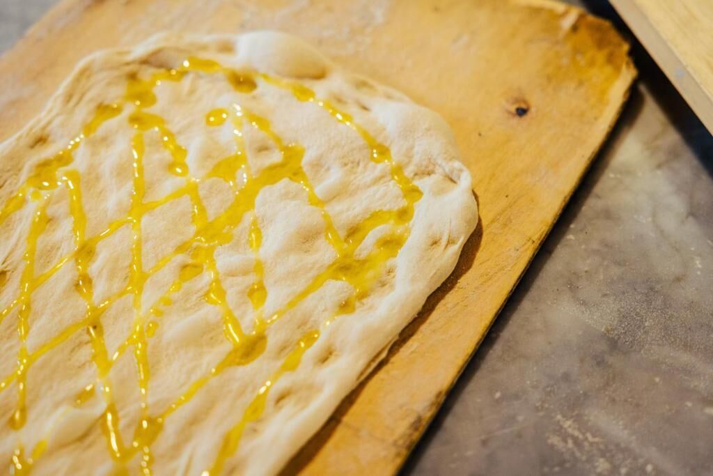 Litteä leipä, jonka päälle on lorautettu keltaista kastiketta, ja se on asetettu puulautalle.