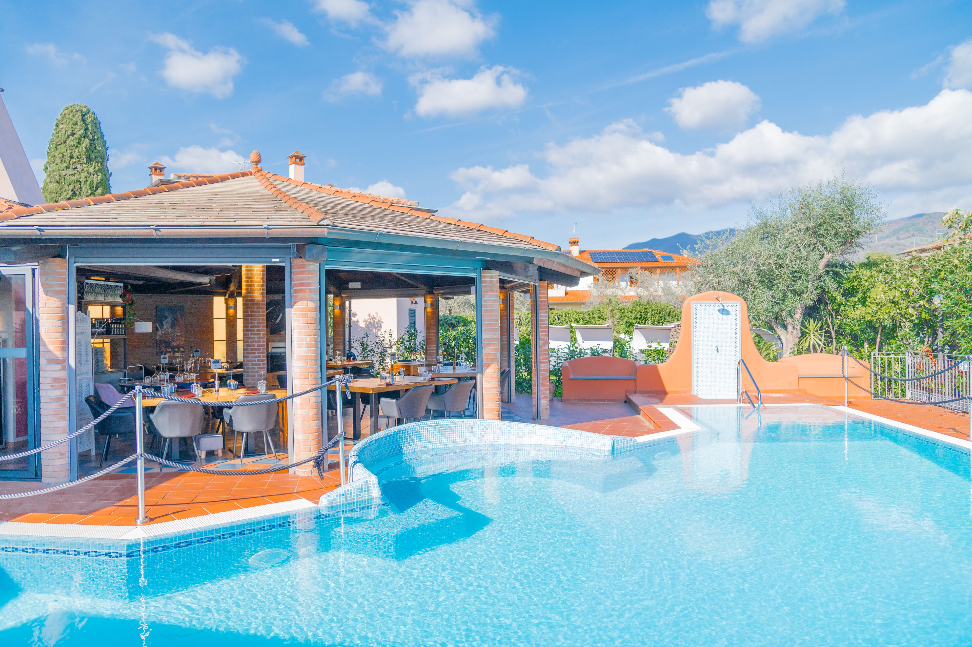 A poolside area with a covered seating area, a dining setup, and a view of the surrounding landscape.