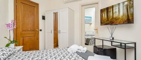 A hotel room with a large bed, a desk, a mirror, and a painting on the wall.